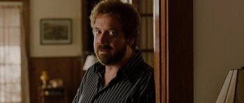 Movie still from “Barney's Version” (2010), directed by Richard J. Lewis – A man with a beard is standing in a room; Close Up shot, Over the shoulder angle