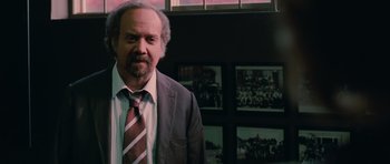 Movie still from “Barney's Version” (2010), directed by Richard J. Lewis – A man in a suit and tie standing in front of pictures; Medium shot, Over the shoulder angle