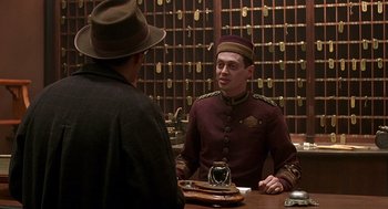Movie still from “Barton Fink” (1991), directed by Joel Coen – A man wearing a hat and a uniform talking to another man in a hat; Medium shot, Over the shoulder angle