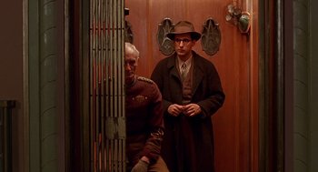 Movie still from “Barton Fink” (1991), directed by Joel Coen – A man in a suit and hat standing next to another man in a suit; Medium shot, Low angle