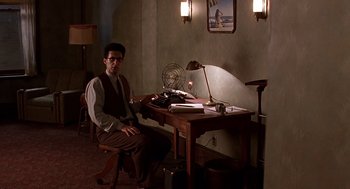 Movie still from “Barton Fink” (1991), directed by Joel Coen – A man sitting at a desk in front of a lamp; Wide shot, High angle