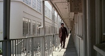 Movie still from “Barton Fink” (1991), directed by Joel Coen – A man in a suit and sunglasses walking down a sidewalk; Wide shot, High angle