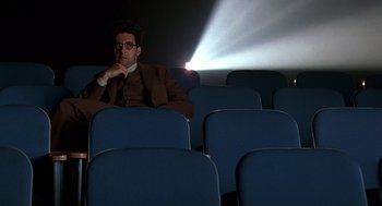 Movie still from “Barton Fink” (1991), directed by Joel Coen – A man sitting in a movie theater with his hand under his chin; Wide shot, Low angle