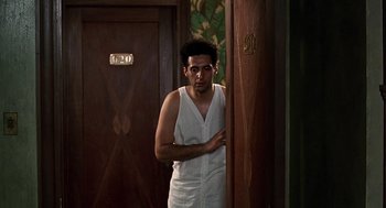 Movie still from “Barton Fink” (1991), directed by Joel Coen – A man standing in front of a door in a room; Medium shot, Low angle