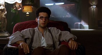 Movie still from “Barton Fink” (1991), directed by Joel Coen – A man sitting in a chair with his hands on his hips; Medium shot, Low angle