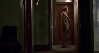 Movie still from “Barton Fink” (1991), directed by Joel Coen – A man standing in front of an open door; Wide shot, Low angle