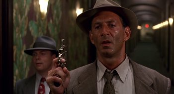 Movie still from “Barton Fink” (1991), directed by Joel Coen – A man in a suit and hat holding a gun; Close Up shot, Low angle