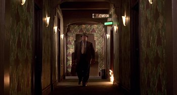 Movie still from “Barton Fink” (1991), directed by Joel Coen – A man in a suit and tie walking down a hall way; Wide shot, Low angle