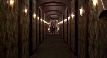 Movie still from “Barton Fink” (1991), directed by Joel Coen – A person is standing in a hallway with lights on; Wide shot, High angle