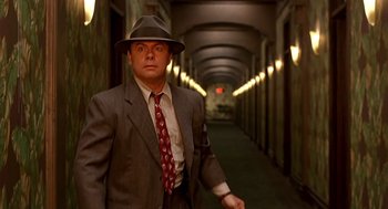 Movie still from “Barton Fink” (1991), directed by Joel Coen – A man in a suit and hat standing in a hallway; Medium shot, Low angle