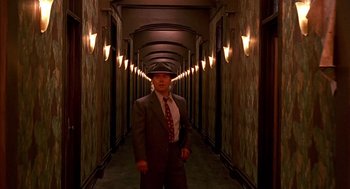 Movie still from “Barton Fink” (1991), directed by Joel Coen – A man in a suit and tie standing in a hallway; Wide shot, High angle