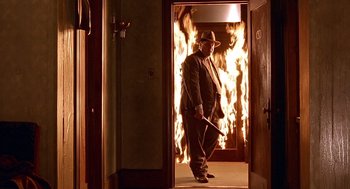 Movie still from “Barton Fink” (1991), directed by Joel Coen – A man standing in front of a fire in a room; Wide shot, Low angle