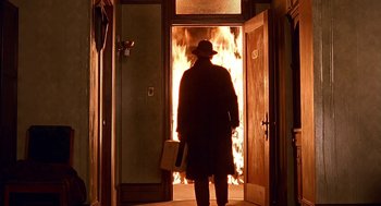 Movie still from “Barton Fink” (1991), directed by Joel Coen – A man standing in front of a fire in a doorway; Wide shot, Low angle