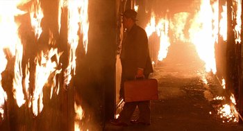 Movie still from “Barton Fink” (1991), directed by Joel Coen – A man with a suitcase walking in front of a fire; Wide shot, High angle