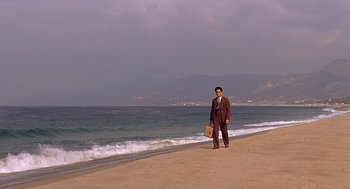 Movie still from “Barton Fink” (1991), directed by Joel Coen – A man standing on the beach holding a briefcase; Extreme Wide shot, High angle