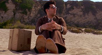 Movie still from “Barton Fink” (1991), directed by Joel Coen – A man sitting on the ground with his hands crossed; Medium shot, Low angle