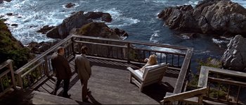 Movie still from “Basic Instinct” (1992), directed by Paul Verhoeven – A man and a woman sitting on a bench near the ocean; Extreme Wide shot, High angle