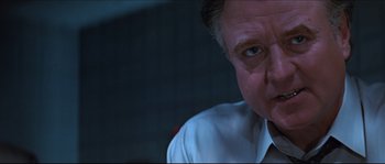 Movie still from “Basic Instinct” (1992), directed by Paul Verhoeven – An older man wearing a white dress shirt and tie; Close Up shot, Low angle