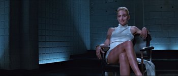 Movie still from “Basic Instinct” (1992), directed by Paul Verhoeven – A woman sitting on top of a chair in a room; Medium shot, Low angle