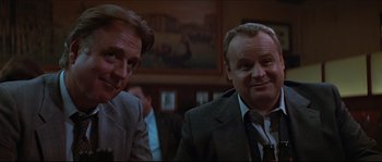 Movie still from “Basic Instinct” (1992), directed by Paul Verhoeven – Two men in suits and ties sitting next to each other; Close Up shot, Low angle