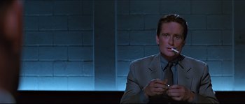 Movie still from “Basic Instinct” (1992), directed by Paul Verhoeven – A man in a suit and tie smoking a cigarette; Medium shot, Low angle