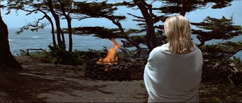 Movie still from “Basic Instinct” (1992), directed by Paul Verhoeven – A woman standing in front of a fire on a beach; Wide shot, Over the shoulder angle