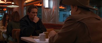 Movie still from “Basic Instinct” (1992), directed by Paul Verhoeven – A man sitting at a table in front of another man; Medium shot, Over the shoulder angle