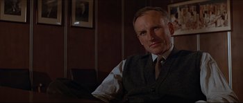 Movie still from “Basic Instinct” (1992), directed by Paul Verhoeven – A man sitting in a chair wearing a vest and a tie; Close Up shot, Low angle