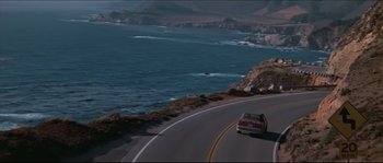 Movie still from “Basic Instinct” (1992), directed by Paul Verhoeven – A car driving down a road next to a body of water; Extreme Wide shot, High angle