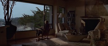 Movie still from “Basic Instinct” (1992), directed by Paul Verhoeven – A man sitting in a rocking chair in front of a large window; Wide shot, High angle