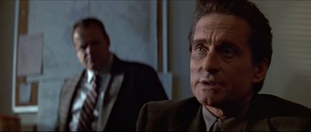 Movie still from “Basic Instinct” (1992), directed by Paul Verhoeven – A man in a suit and tie sitting next to another man in a suit and tie; Close Up shot, Over the shoulder angle