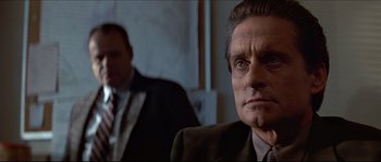 Movie still from “Basic Instinct” (1992), directed by Paul Verhoeven – A man in a suit and tie sitting in front of another man; Close Up shot, Over the shoulder angle