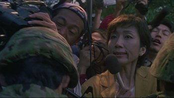 Movie still from “Battle Royale” (2000), directed by Kinji Fukasaku – A group of people gathered around a microphone; Close Up shot, High angle