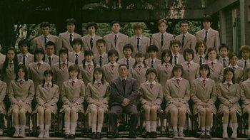 Movie still from “Battle Royale” (2000), directed by Kinji Fukasaku – A group of people in suits and ties sitting and standing; Wide shot, High angle