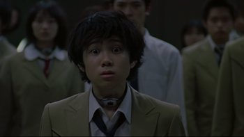 Movie still from “Battle Royale” (2000), directed by Kinji Fukasaku – A man in a suit and tie looking at the camera; Close Up shot, Low angle