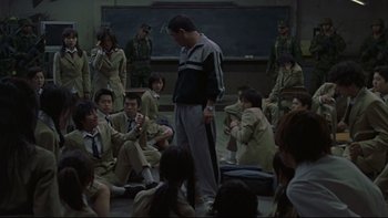 Movie still from “Battle Royale” (2000), directed by Kinji Fukasaku – A group of people sitting in a room; Wide shot, High angle