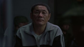 Movie still from “Battle Royale” (2000), directed by Kinji Fukasaku – An older man in a black and white jacket; Close Up shot, Over the shoulder angle