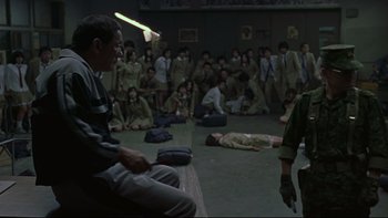 Movie still from “Battle Royale” (2000), directed by Kinji Fukasaku – A group of people sitting in a room; Wide shot, High angle