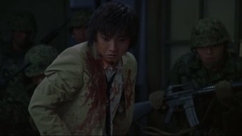 Movie still from “Battle Royale” (2000), directed by Kinji Fukasaku – A man with blood on his face and a gun in his hand; Medium shot, Over the shoulder angle