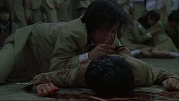 Movie still from “Battle Royale” (2000), directed by Kinji Fukasaku – A man in military fatigues is wrestling another man; Medium shot, High angle