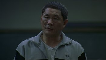 Movie still from “Battle Royale” (2000), directed by Kinji Fukasaku – An older asian man in a gray jacket; Close Up shot, High angle
