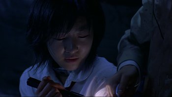 Movie still from “Battle Royale” (2000), directed by Kinji Fukasaku – A young girl looking down at her cell phone in the dark; Close Up shot, High angle