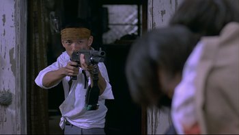 Movie still from “Battle Royale” (2000), directed by Kinji Fukasaku – A man holding a gun in front of a mirror; Medium shot, Low angle