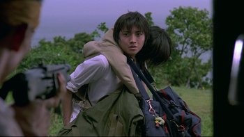 Movie still from “Battle Royale” (2000), directed by Kinji Fukasaku – A man carrying a woman on his back while holding a gun; Medium shot, Over the shoulder angle