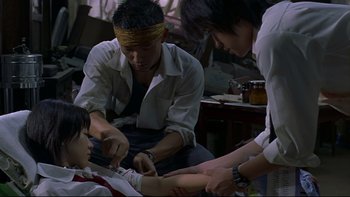 Movie still from “Battle Royale” (2000), directed by Kinji Fukasaku – A group of people sitting on the ground; Medium shot, High angle