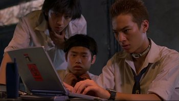 Movie still from “Battle Royale” (2000), directed by Kinji Fukasaku – A group of young men sitting at a table looking at a computer; Close Up shot, Low angle