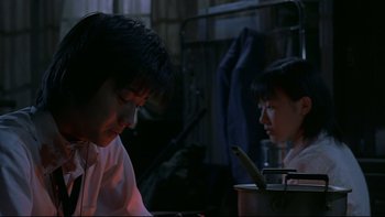 Movie still from “Battle Royale” (2000), directed by Kinji Fukasaku – Two people sitting at a table looking at a phone; Medium shot, Over the shoulder angle