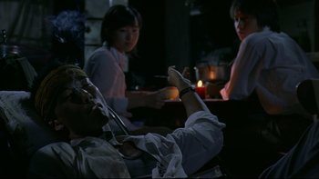 Movie still from “Battle Royale” (2000), directed by Kinji Fukasaku – Three people sitting at a table in front of candles; Medium shot, Low angle