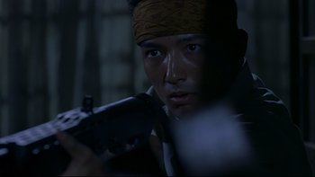 Movie still from “Battle Royale” (2000), directed by Kinji Fukasaku – A man holding a gun while wearing bandanas; Close Up shot, Low angle