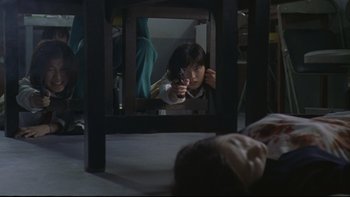 Movie still from “Battle Royale” (2000), directed by Kinji Fukasaku – A woman holding a gun in front of a mirror; Medium shot, High angle
